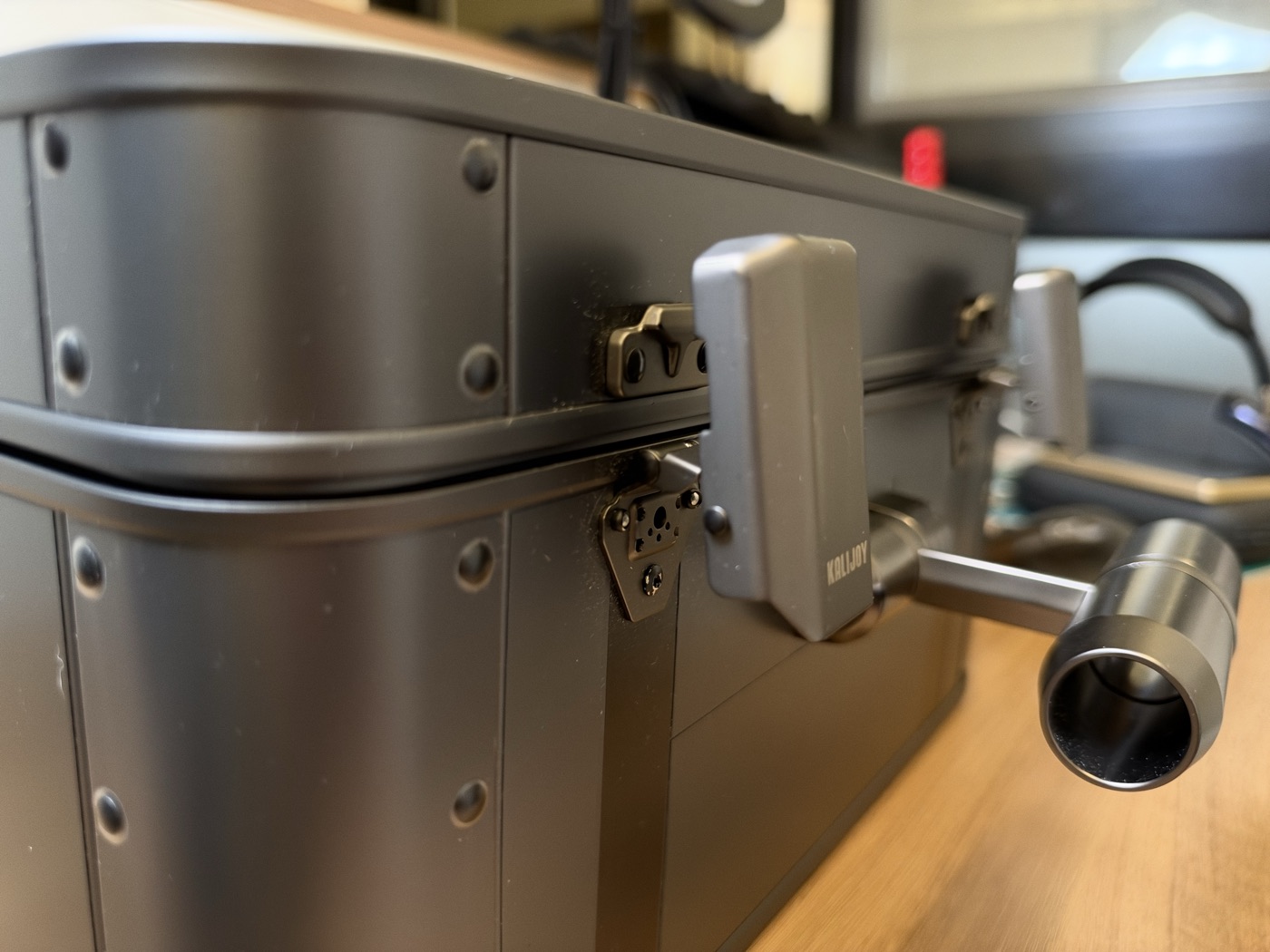 Close-up of the Kalijoy K CASE hinge, side latch and the stainless steel handle post, showing brushed metal and rivets.