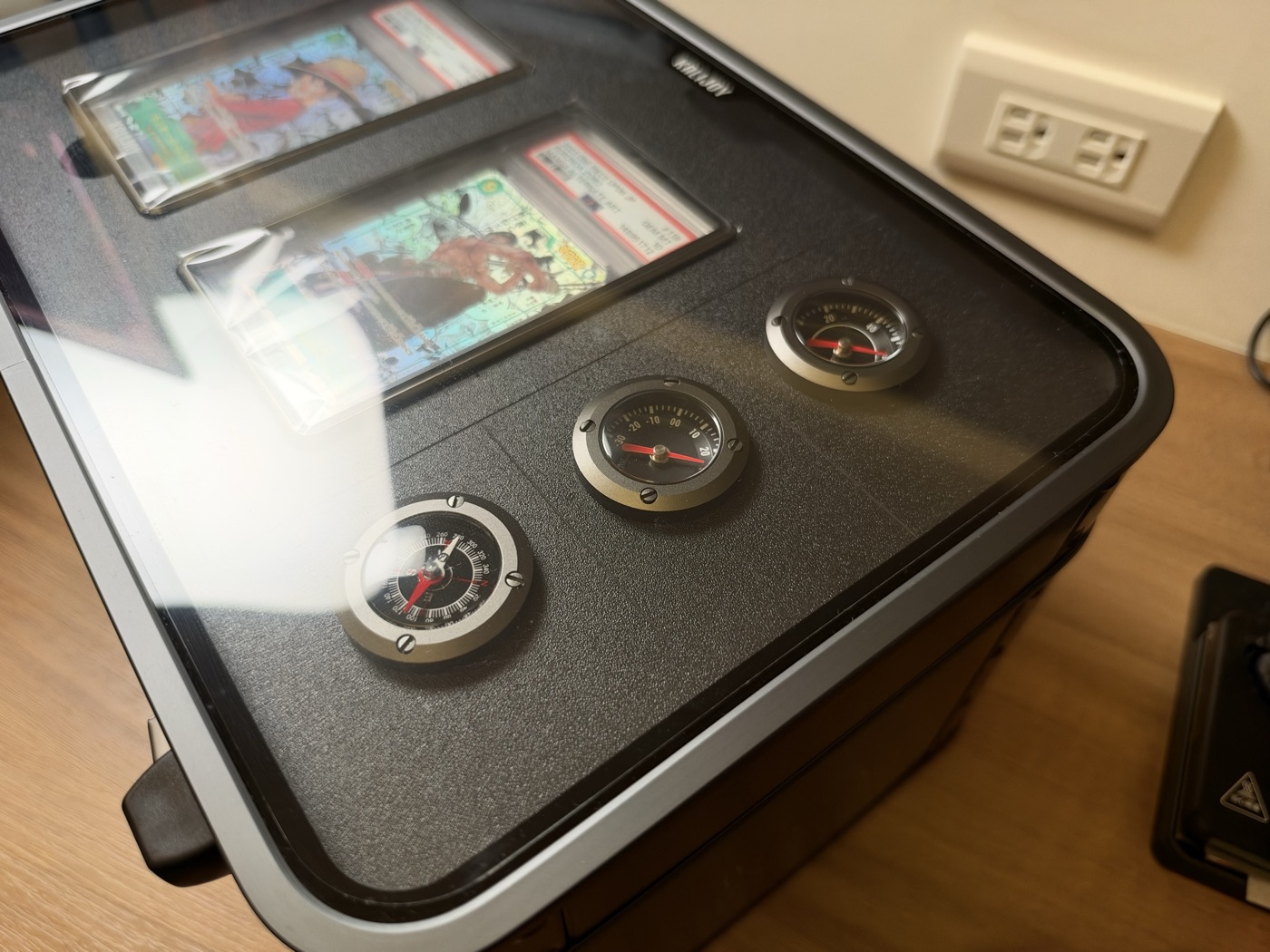 Close-up of the three round gauges on the Kalijoy K CASE front panel: a compass, a thermometer and a hygrometer.