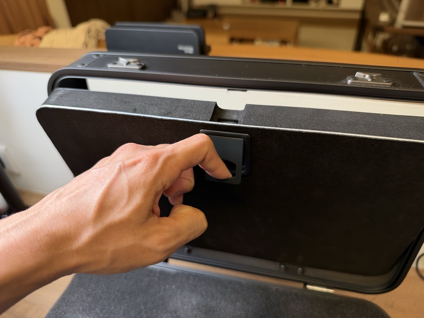 A hand releasing the front panel catch on the Kalijoy K CASE so the display panel folds down.